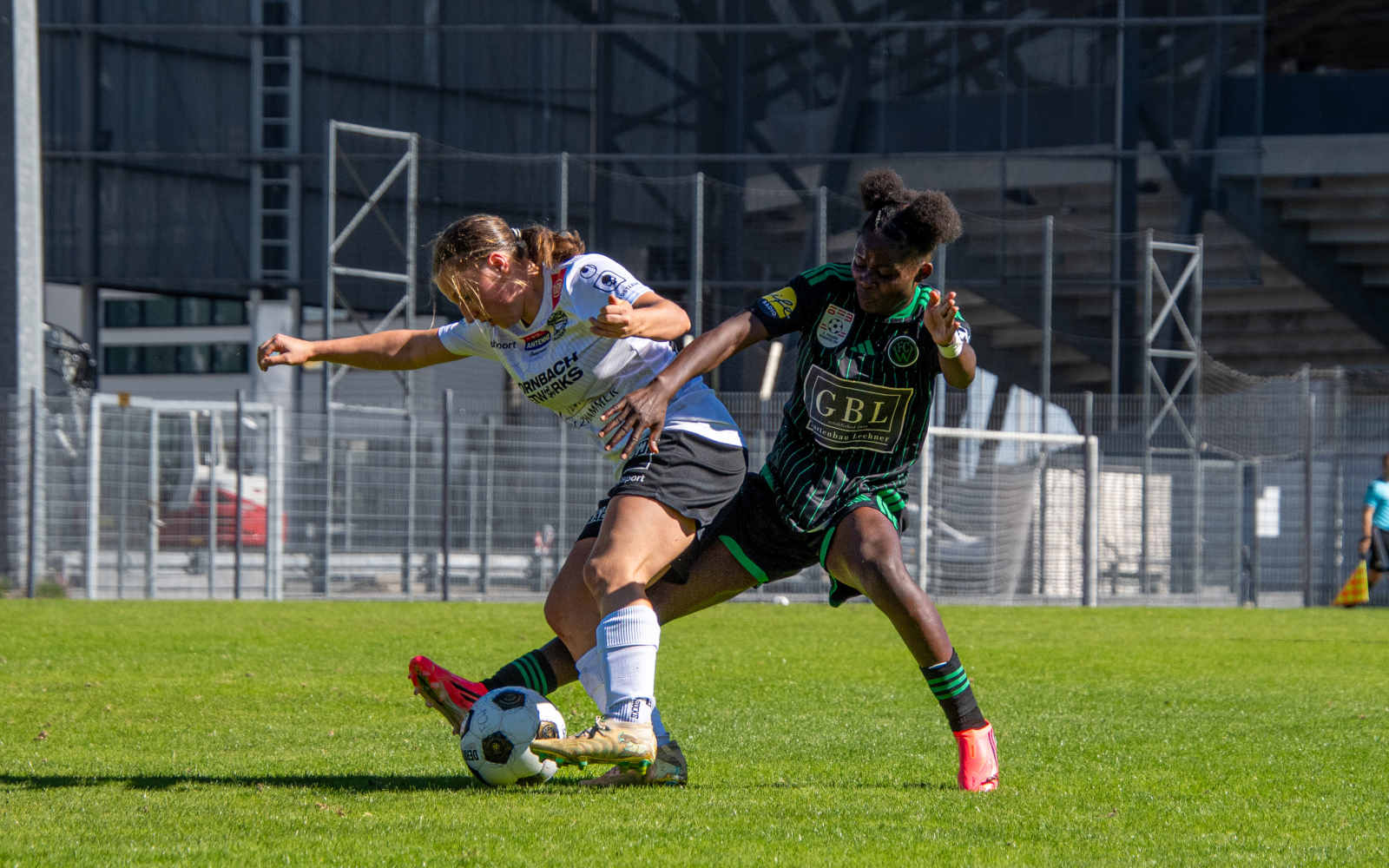 Fußballerinnen im Zweikampf auf Rasen vor Tribüne und Stadion